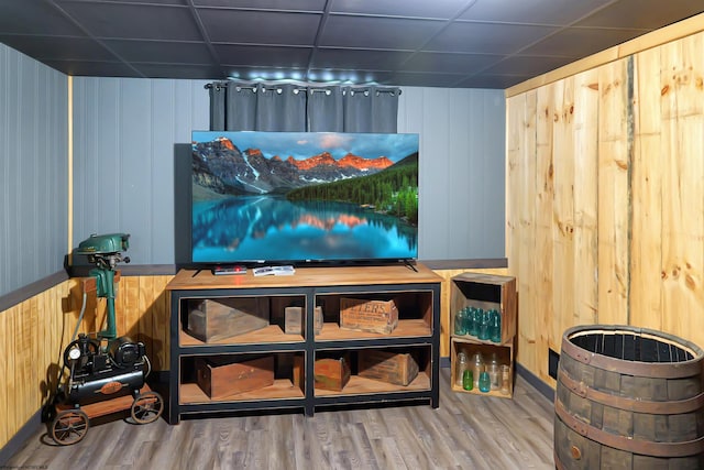 interior space with a drop ceiling, wood walls, and hardwood / wood-style floors