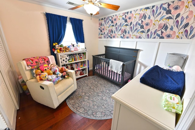 bedroom featuring crown molding, dark wood-type flooring, ceiling fan, and a nursery area