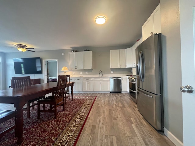 kitchen featuring appliances with stainless steel finishes, light hardwood / wood-style floors, white cabinets, ceiling fan, and sink