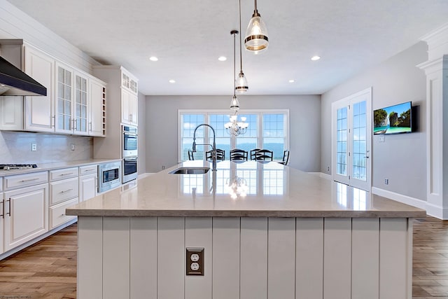 kitchen featuring an island with sink, white cabinets, light wood-type flooring, decorative light fixtures, and sink