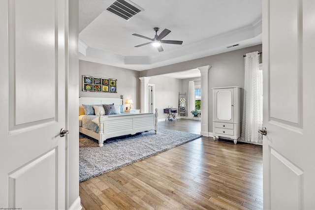 bedroom featuring ornate columns, a raised ceiling, ceiling fan, and hardwood / wood-style flooring