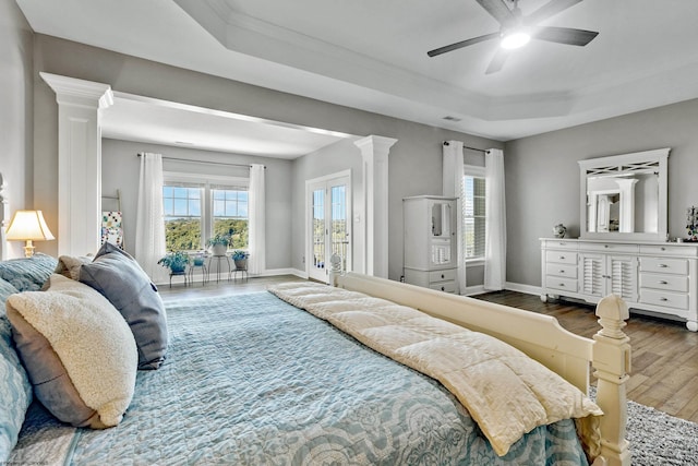 bedroom with ceiling fan, a raised ceiling, hardwood / wood-style flooring, crown molding, and ornate columns