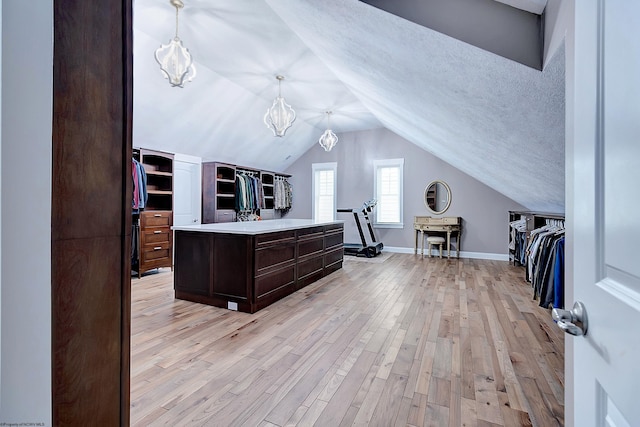 kitchen featuring dark brown cabinets, light hardwood / wood-style floors, a textured ceiling, vaulted ceiling, and hanging light fixtures