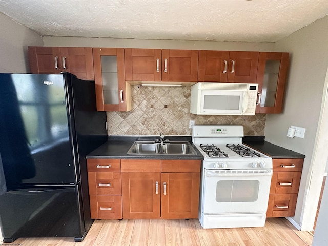 kitchen featuring a sink, brown cabinetry, white appliances, dark countertops, and light wood-style floors