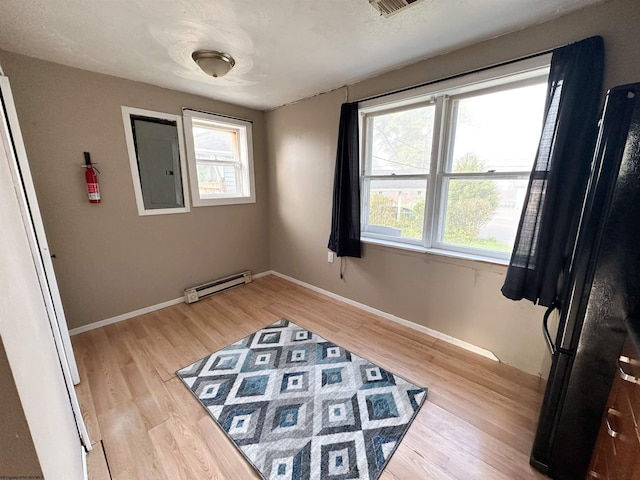 bedroom featuring black fridge, light hardwood / wood-style floors, electric panel, and a baseboard heating unit