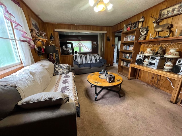 living room featuring wood walls, ceiling fan, light colored carpet, and a textured ceiling