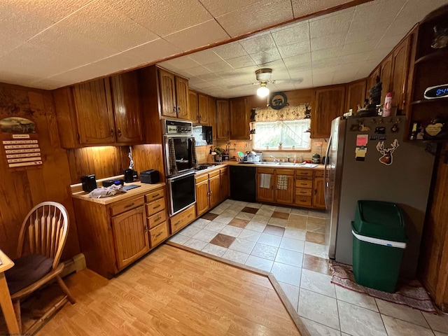 kitchen featuring light hardwood / wood-style flooring, black appliances, ceiling fan, and wood walls