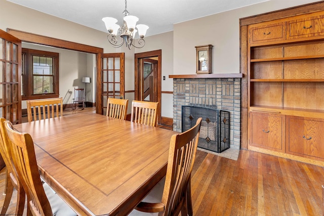 dining room featuring wood-type flooring, an inviting chandelier, and a brick fireplace