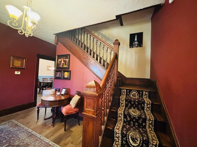 staircase with a chandelier, a textured ceiling, and hardwood / wood-style flooring