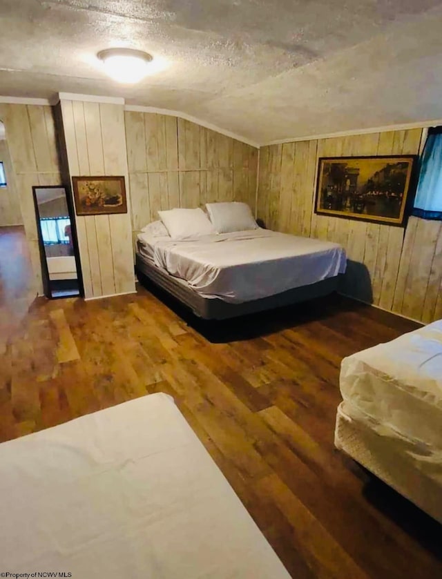 bedroom with lofted ceiling, a textured ceiling, wood walls, and dark hardwood / wood-style flooring