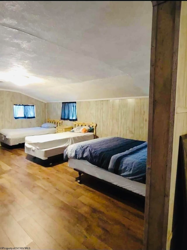 bedroom with lofted ceiling, wood walls, and hardwood / wood-style floors