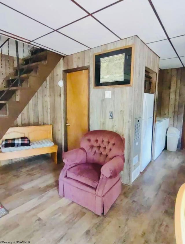 living area featuring hardwood / wood-style flooring, wood walls, and a paneled ceiling