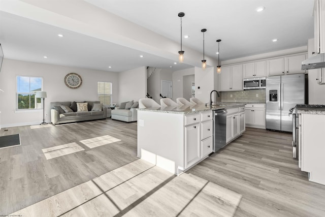 kitchen with hanging light fixtures, an island with sink, stainless steel appliances, and white cabinets