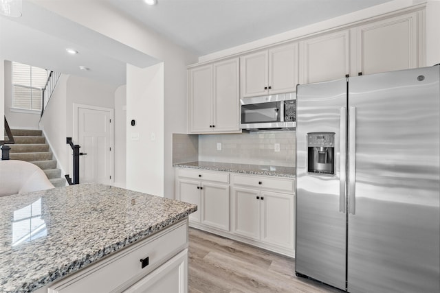 kitchen with light hardwood / wood-style floors, tasteful backsplash, white cabinetry, appliances with stainless steel finishes, and light stone countertops