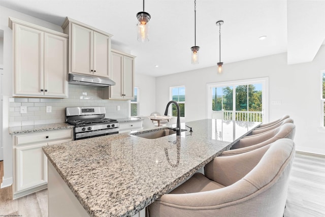 kitchen with light stone counters, light hardwood / wood-style floors, sink, stainless steel gas range oven, and decorative light fixtures