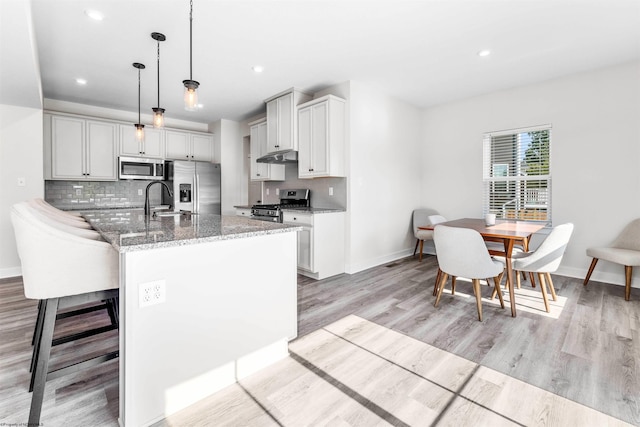 kitchen featuring light wood-type flooring, appliances with stainless steel finishes, hanging light fixtures, and stone countertops