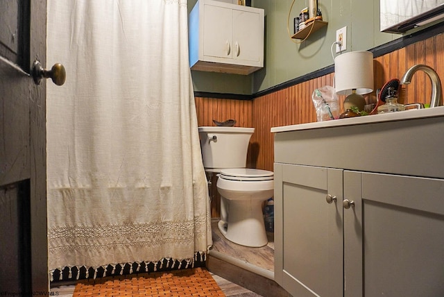 bathroom with wood walls, walk in shower, vanity, and toilet