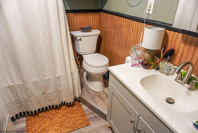 bathroom with hardwood / wood-style floors, wooden walls, toilet, and vanity