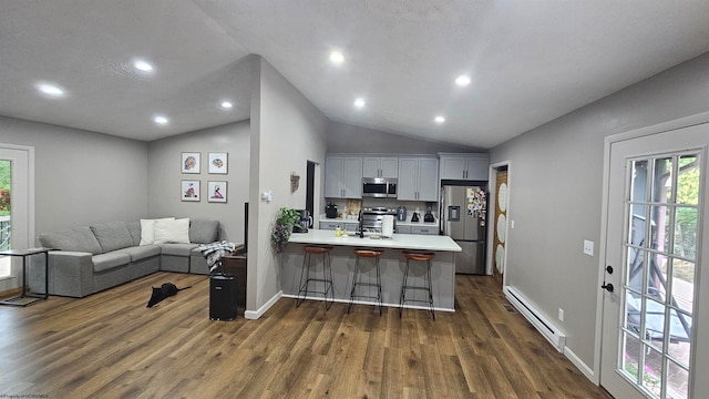 kitchen featuring a breakfast bar, kitchen peninsula, vaulted ceiling, appliances with stainless steel finishes, and a baseboard radiator