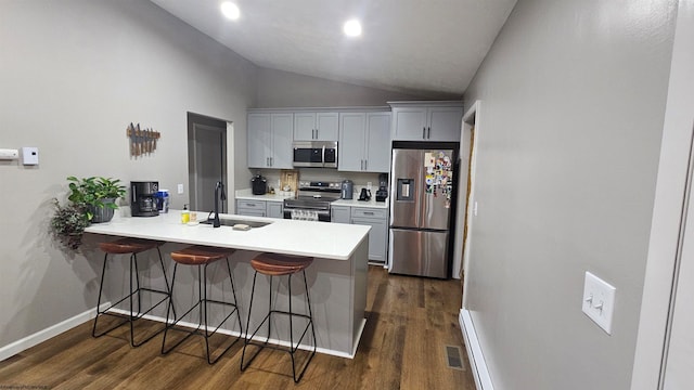 kitchen with gray cabinetry, a breakfast bar area, dark wood-type flooring, vaulted ceiling, and stainless steel appliances