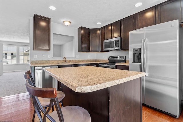 kitchen featuring a breakfast bar, wood-type flooring, dark brown cabinets, appliances with stainless steel finishes, and a center island