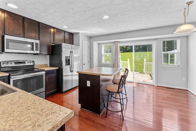 kitchen featuring appliances with stainless steel finishes, dark wood-type flooring, hanging light fixtures, and a center island