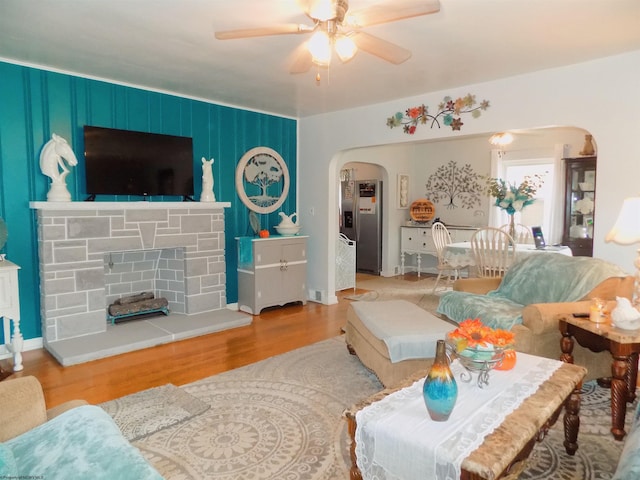 living room featuring ceiling fan, a stone fireplace, and light hardwood / wood-style flooring