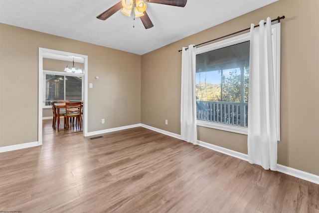 spare room with ceiling fan with notable chandelier and light hardwood / wood-style floors