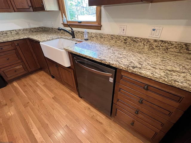 kitchen with light stone countertops, light wood finished floors, stainless steel dishwasher, and a sink