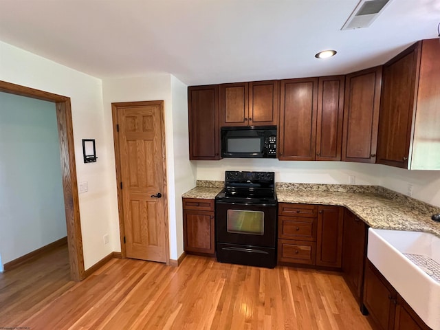 kitchen featuring light wood-type flooring, black appliances, sink, and light stone countertops