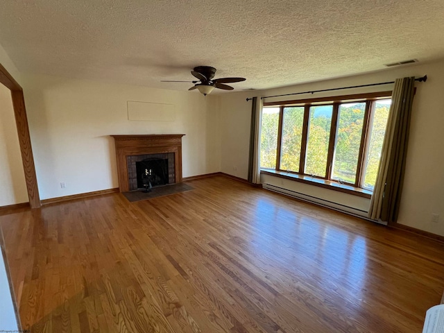 unfurnished living room with ceiling fan, hardwood / wood-style floors, a fireplace, a baseboard radiator, and a textured ceiling