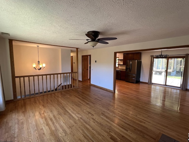 unfurnished living room featuring baseboards, a textured ceiling, dark wood-type flooring, and ceiling fan with notable chandelier