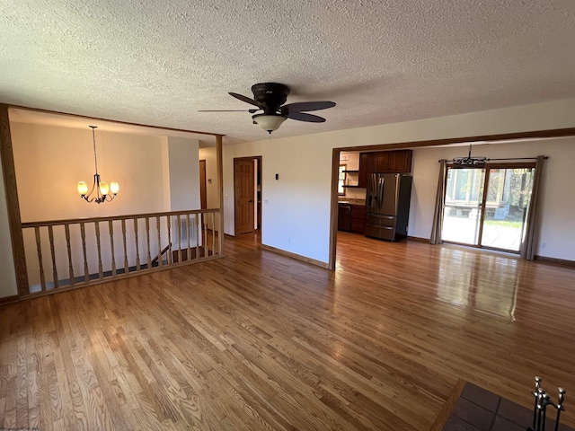 unfurnished living room featuring dark wood-type flooring, a textured ceiling, and ceiling fan with notable chandelier