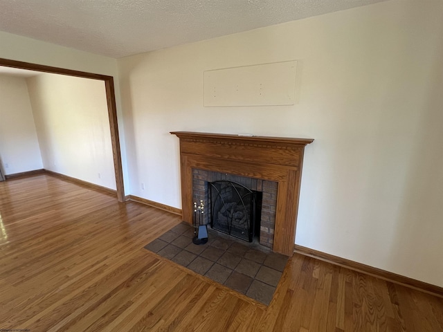 unfurnished living room with a textured ceiling, wood finished floors, a brick fireplace, and baseboards