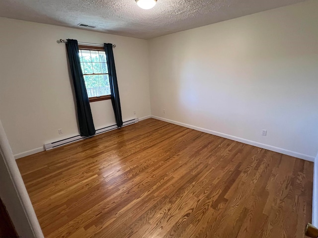 empty room with hardwood / wood-style floors, baseboard heating, and a textured ceiling