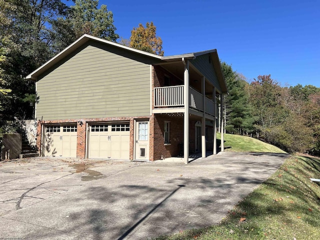 view of side of home with brick siding, an attached garage, driveway, and a balcony