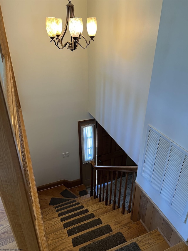 stairs featuring wood finished floors and a chandelier