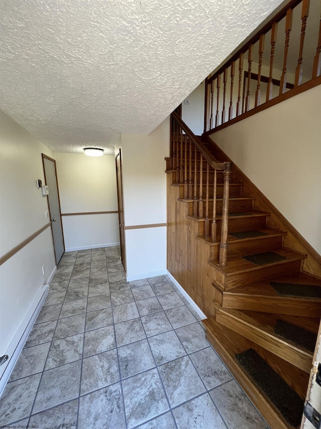 stairs featuring a baseboard heating unit, baseboards, stone tile floors, and a textured ceiling