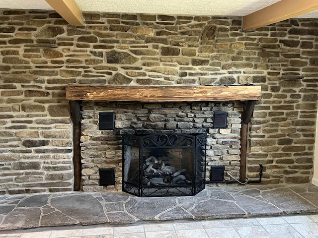 room details with visible vents, a stone fireplace, and beamed ceiling