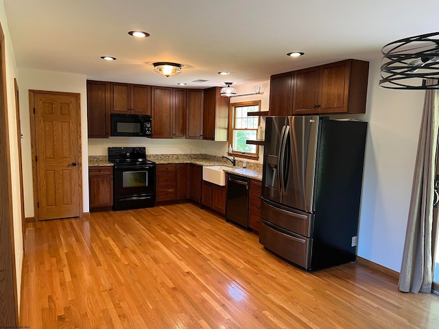 kitchen featuring light stone counters, light hardwood / wood-style flooring, sink, and black appliances