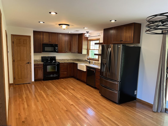 kitchen featuring light wood-type flooring, light stone countertops, a sink, and black appliances