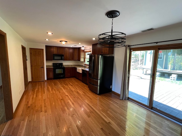 kitchen with decorative light fixtures, light wood-type flooring, a chandelier, and black appliances