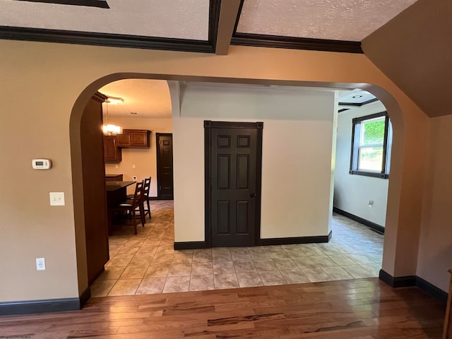 interior space featuring lofted ceiling, crown molding, light hardwood / wood-style flooring, and a textured ceiling