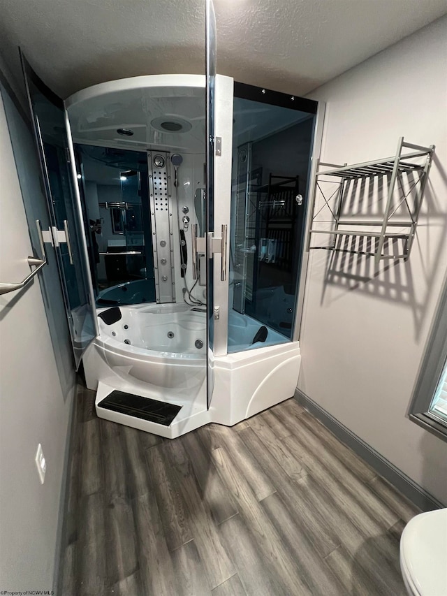 bathroom featuring wood-type flooring, a textured ceiling, plus walk in shower, and toilet