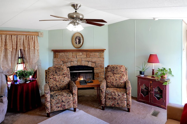 carpeted living room featuring ceiling fan and a stone fireplace