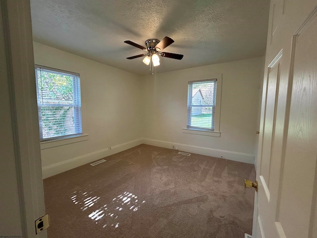 carpeted empty room featuring ceiling fan, plenty of natural light, and a textured ceiling