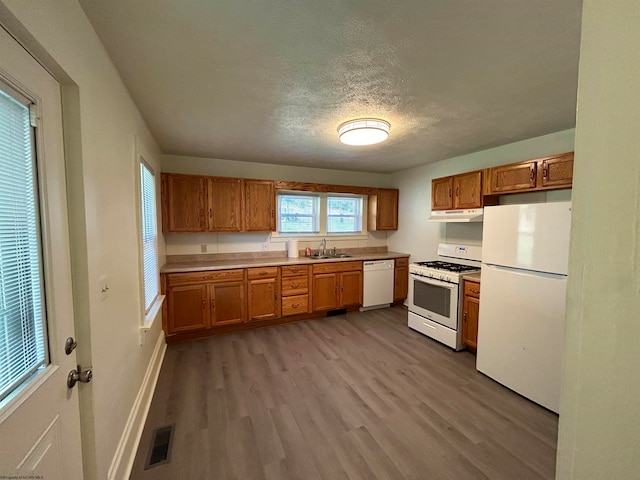 kitchen with light wood-type flooring, white appliances, sink, and a textured ceiling