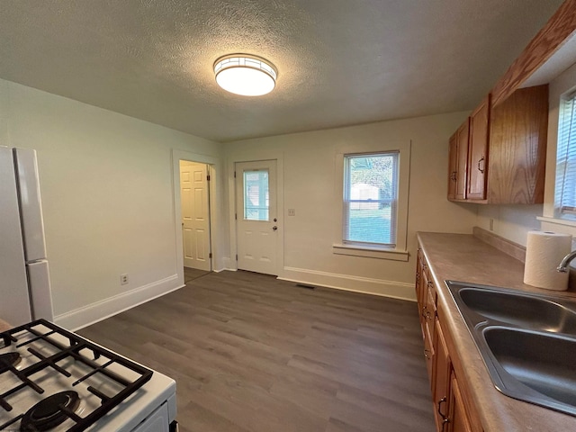 kitchen with stainless steel stove, dark wood-type flooring, sink, white fridge, and a textured ceiling