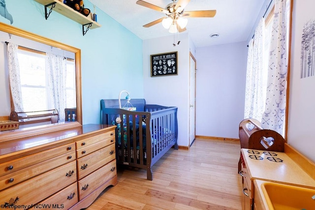 bedroom with sink, light hardwood / wood-style flooring, a nursery area, and ceiling fan