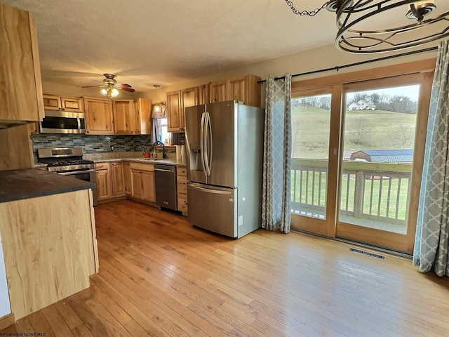 kitchen with ceiling fan, sink, stainless steel appliances, backsplash, and light wood-type flooring